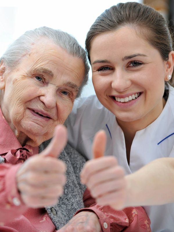 A client and caregiver are smiling at the camera with their thumbs up. Stock Photo: GoDaddy.com