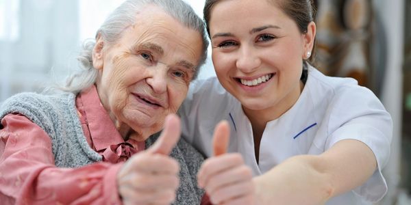 a carer with and elderly woman smiling and giving thumbs up