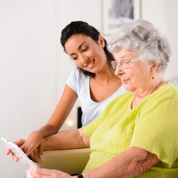A carer helping an elderly woman use a tablet