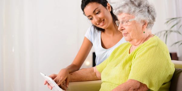 Young woman helping elderly woman use a tablet device.