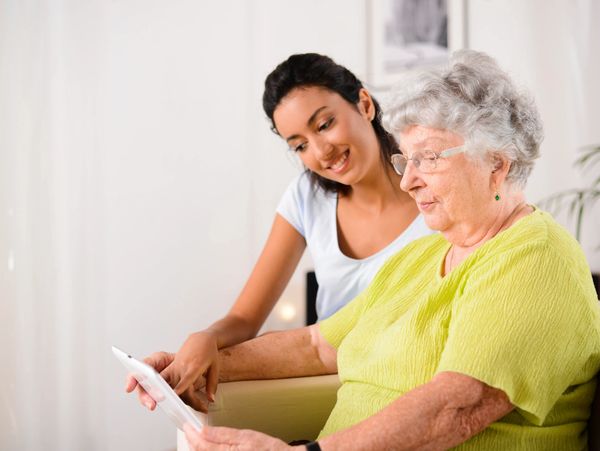 Younger woman helps senior navigate on a computer tablet.