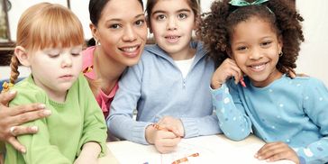 Teacher with three young children engaged in drawing activity.