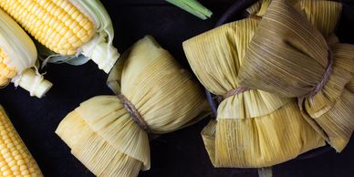 Traditional corn tamales wrapped in corn husks with fresh corn cobs.