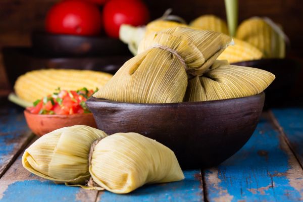 Traditional tamales wrapped in corn husks with salsa on a rustic table.