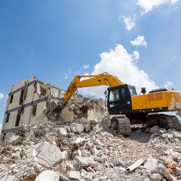 Yellow excavator demolishing a building under clear blue sky.