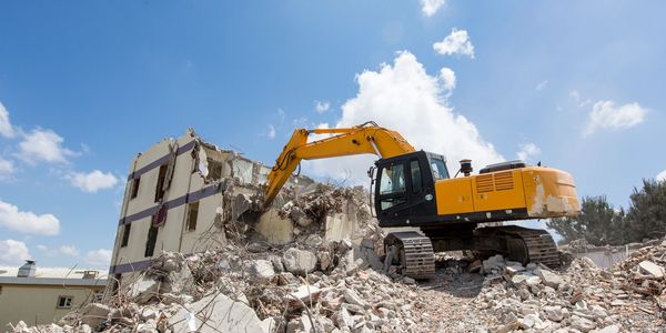 Yellow excavator demolishing a building amid rubble.