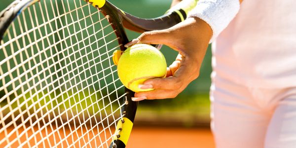 Person holding a tennis ball and racket, ready to serve on clay court.