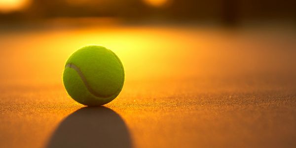 A tennis ball on a court glowing in warm sunset light.