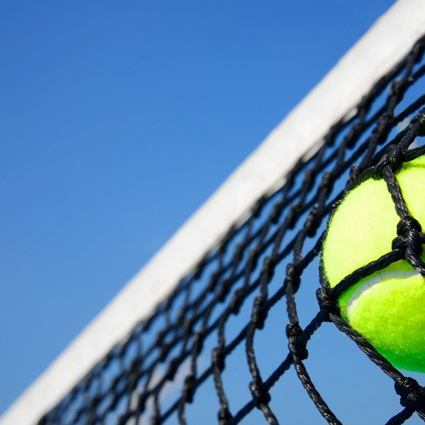 Tennis ball caught in the net against a clear blue sky.