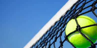 Tennis ball stuck in the net against a clear blue sky.
