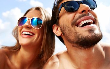 Happy young couple wearing sunglasses outdoors on a sunny day.