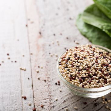 A bowl of mixed quinoa grains on a wooden surface with spinach leaves.