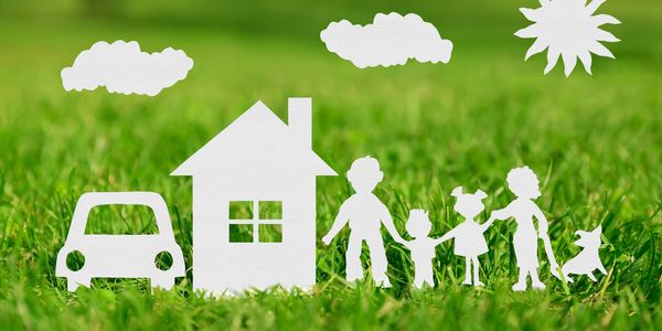 Silhouette image of a family holding hands in the sunshine outside their house.