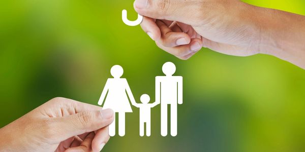 Hands holding paper cutouts of a family under a protective umbrella symbol.