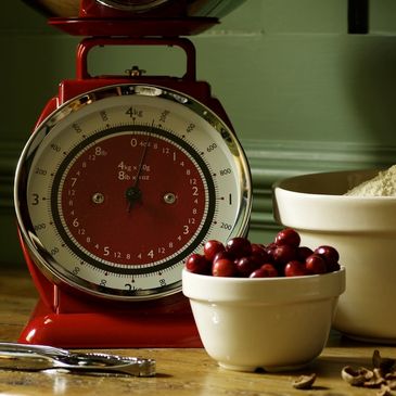 A scale on a wooden table next to cup of dried Cranberry and another full of sesame seeds