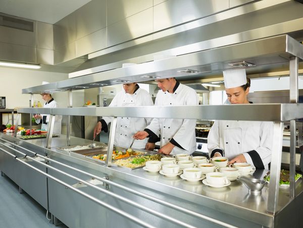 Chefs preparing and serving food in a professional kitchen line.