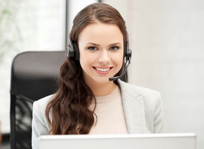 Female client services rep wearing headset at computer. Find answers to frequently asked questions.