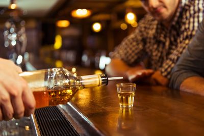 Whiskey being poured into a shot glass at a bar.