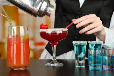 Bartender preparing colorful cocktails and shots at a bar.