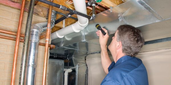 Professional inspecting an air conditioning vent with a flashlight in his hand.