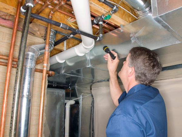 A technician inspects pipes in a basement using a flashlight.