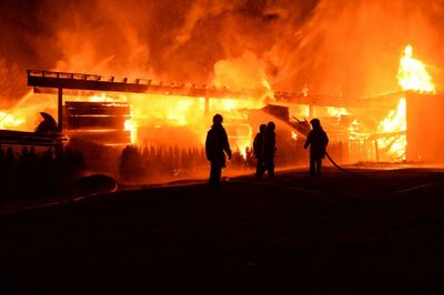 Firefighters battling a large blaze engulfing a wooden structure at night.