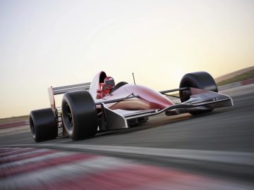 A sleek race car speeds on a track at sunset.