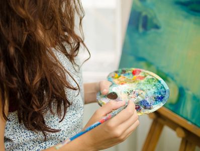 A woman paints with a colorful palette on a canvas.