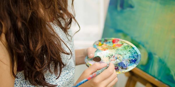 Woman holding paint palette and paintbrush with abstract painting on canvas in the background