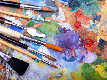 Various paintbrushes on a colorful artist's palette with mixed paints.