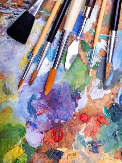 Various paintbrushes and a palette knife on a colorful artist palette.