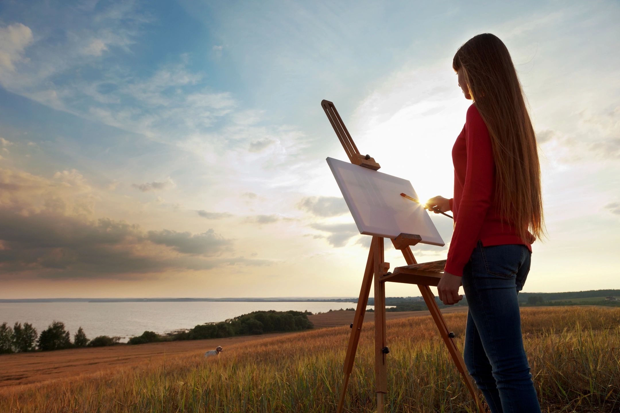 Woman painting on a canvas outdoors during sunset.