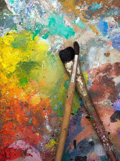 Two paintbrushes lying on a colorful, paint-splattered surface.