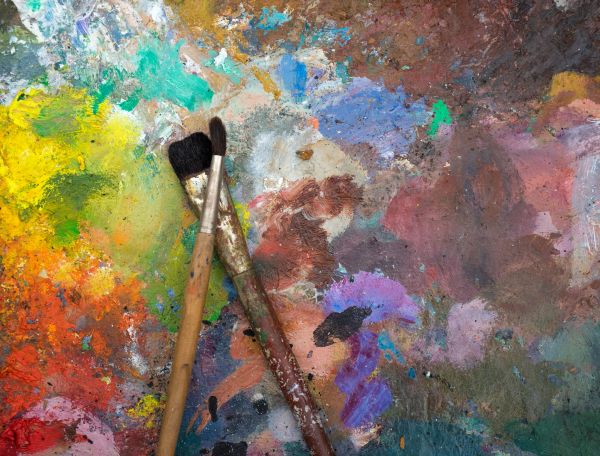Two paintbrushes resting on a colorful, paint-splattered palette.