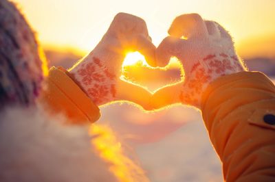 Gloved hands making a heart against a sunset