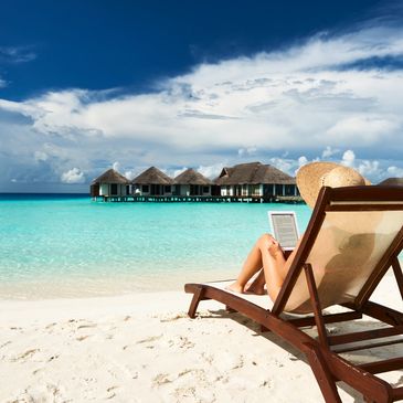 An island getaway in the tropics on a beach and a woman is relaxing in a chair watching the waves.