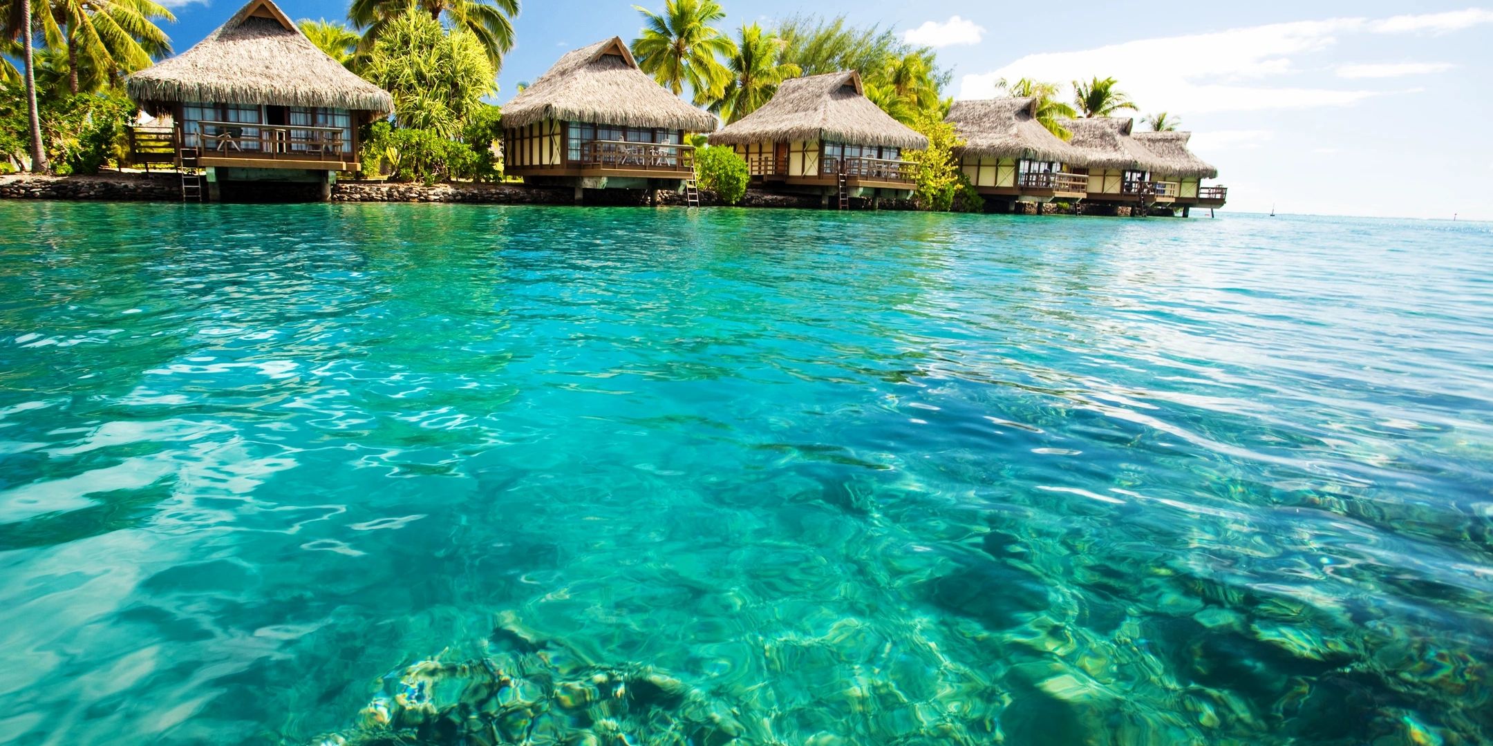 Overwater bungalows on clear turquoise water with lush greenery.