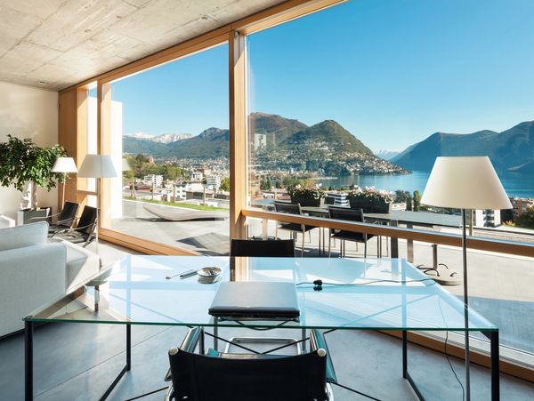 Modern office with glass desk overlooking mountains and lake.
