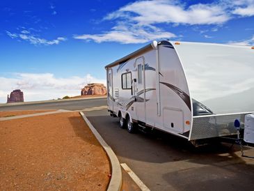 A white travel trailer parked in a desert scenic area under a blue sky.