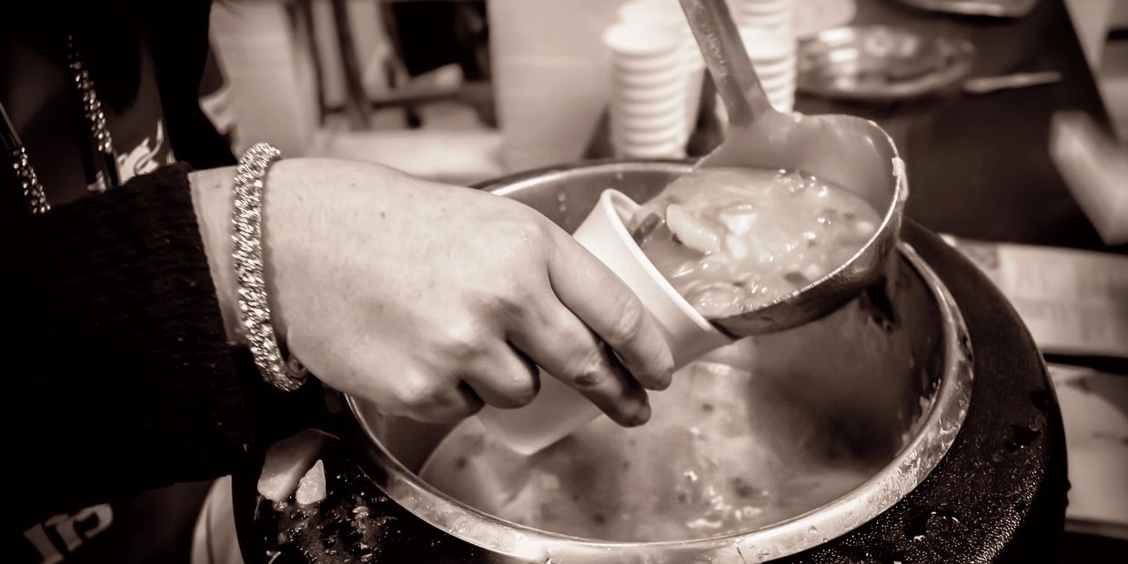 Person ladles soup into a cup from a large pot.