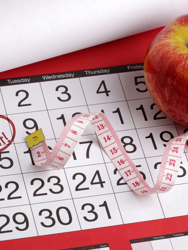 A calendar with a measuring tape and an apple on a red background.