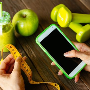 Person recording their waist circumference in their smartphone with green items on a table.
