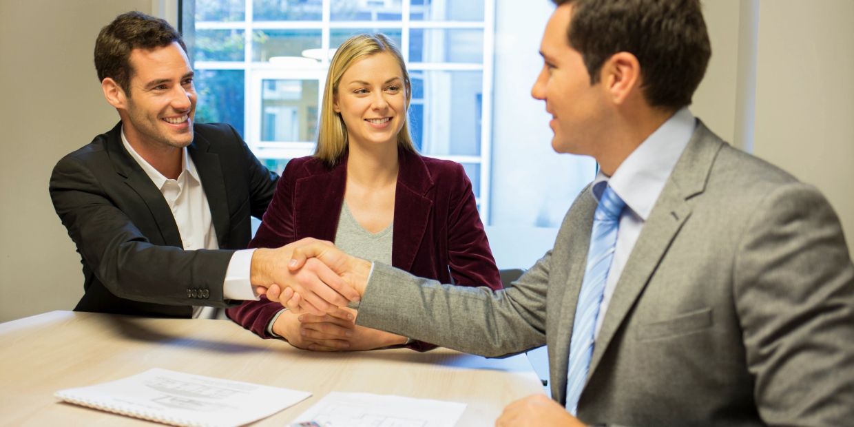 Two men shaking hands over a business deal with a woman watching.