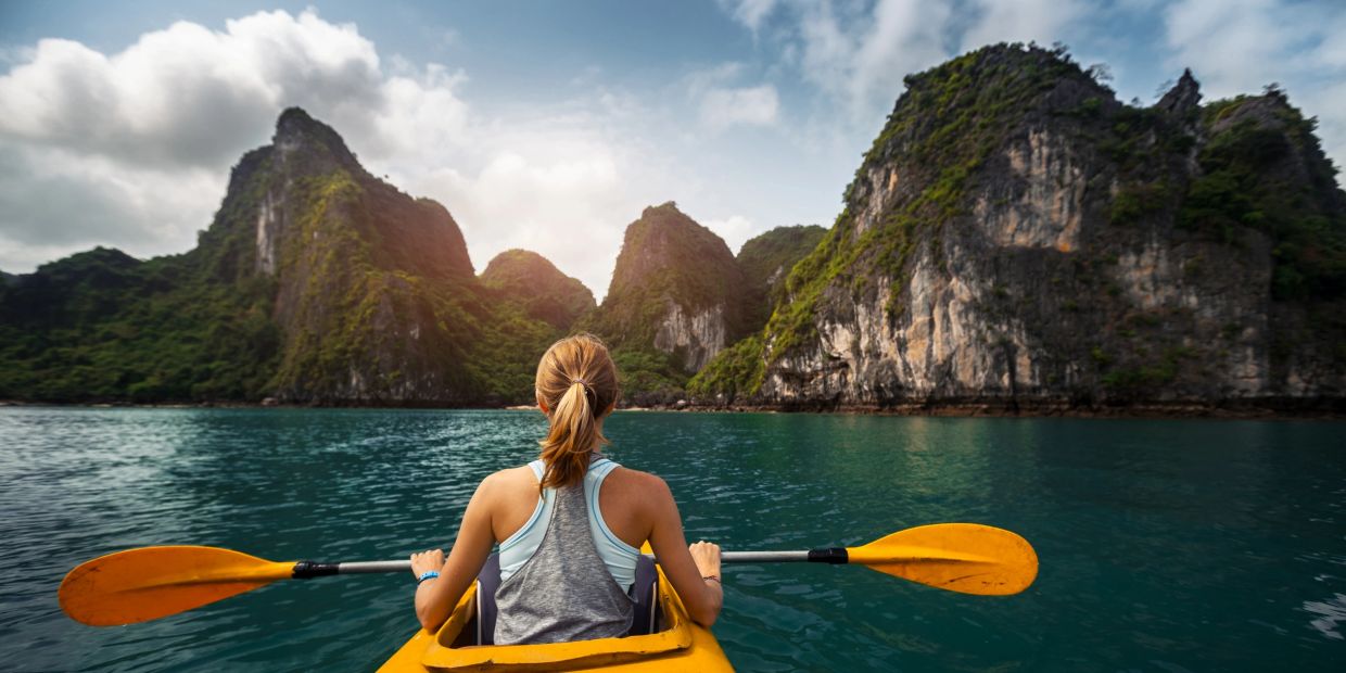 Woman kayaking towards rocky cliffs in calm water.