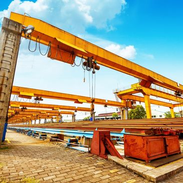 Industrial cranes at a steel manufacturing site under a bright blue sky.