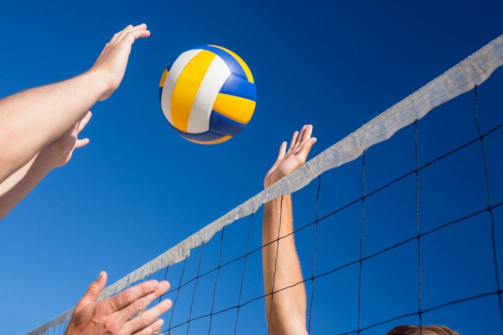 Hands reaching for a volleyball above the net against a clear blue sky.