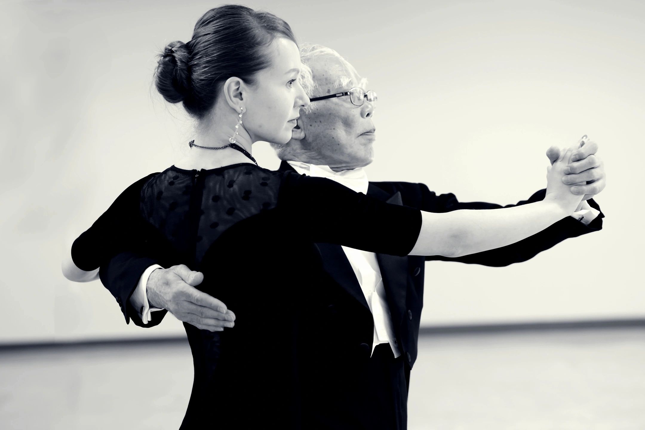 An elderly man and a young woman dancing closely in formal attire.
