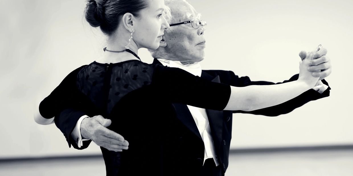 A couple gracefully dancing in formal attire in a black-and-white photo.