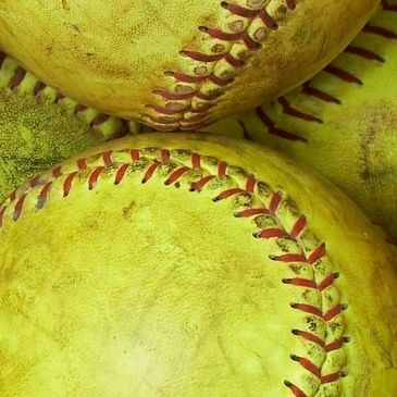 Close-up of worn yellow softballs with red stitching.