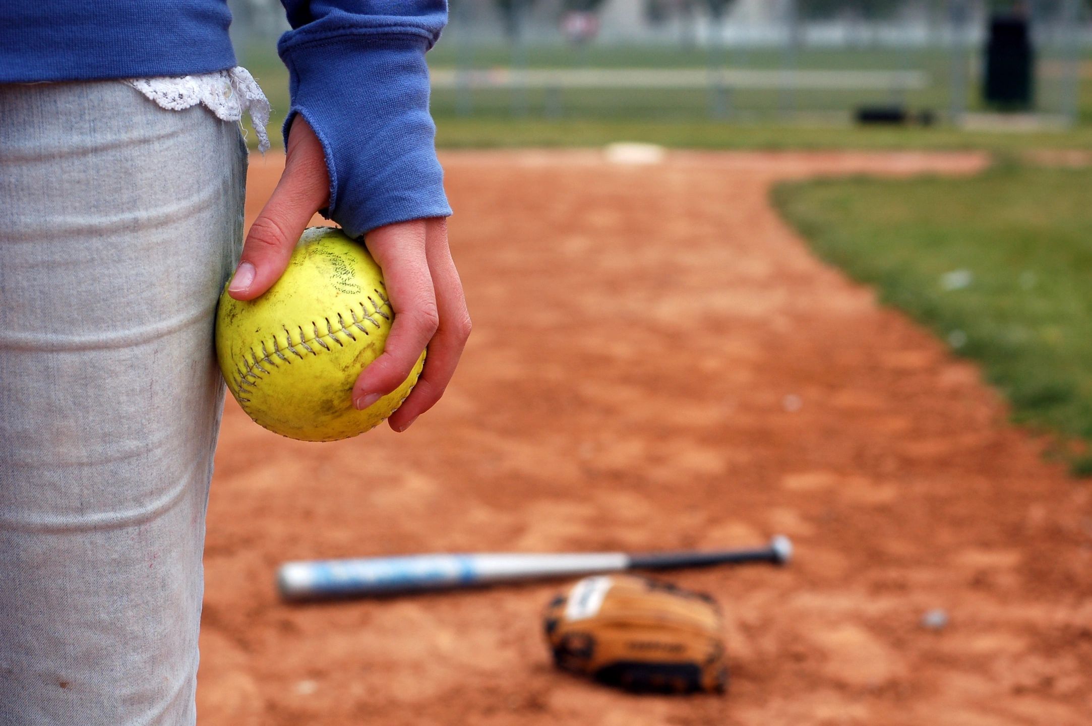 Person holding a softball on a baseball field.